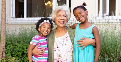 A smiling senior woman with two young girls in a garden