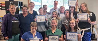Staff members holding Dementia Friends signs in a common area