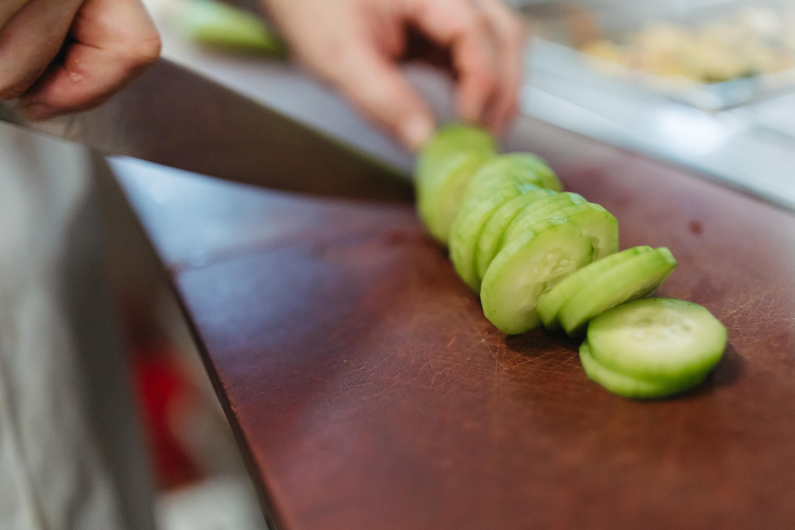 Close-up of a person slicing cucumbers in a kitchen