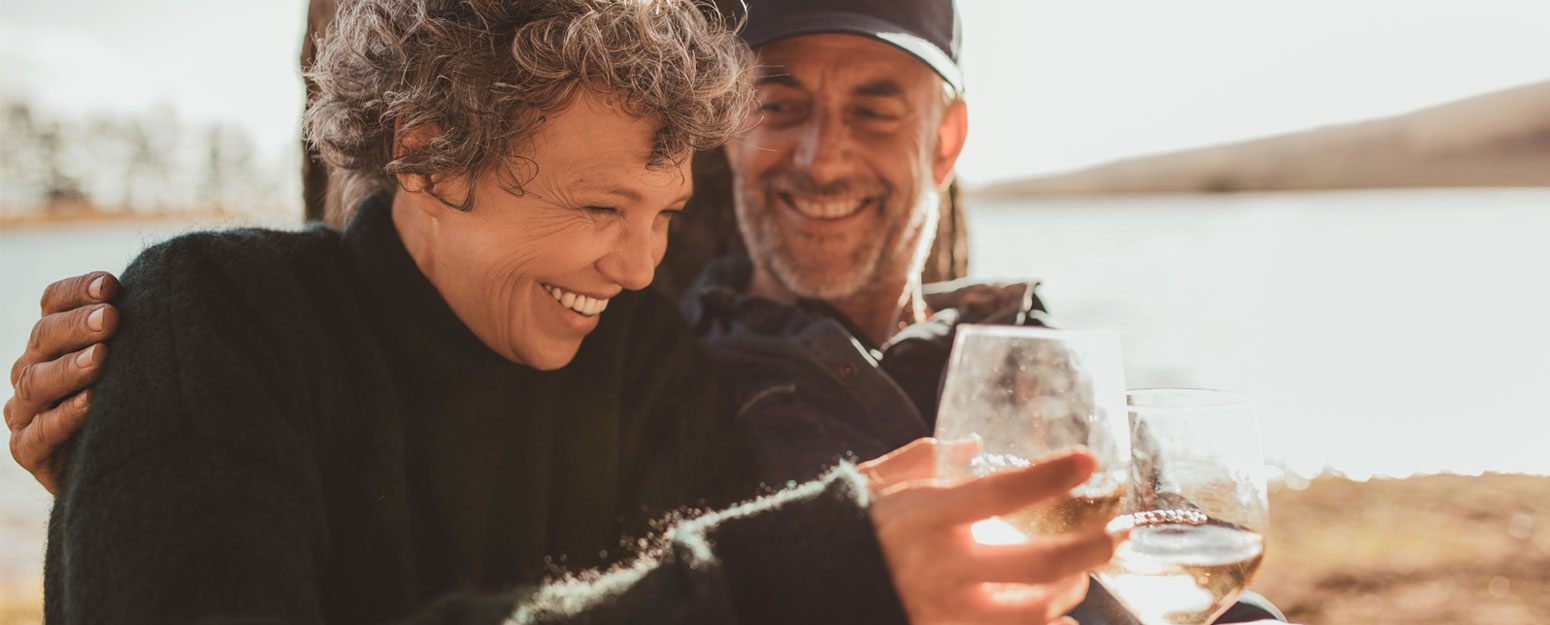 Two seniors enjoying drinks by a lake