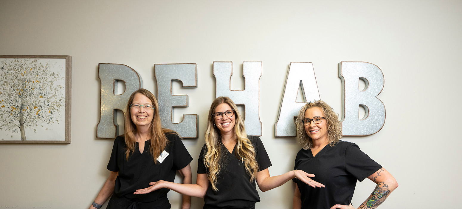 Three staff members posing in front of a 'REHAB' sign