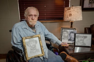 Resident showing framed drawings in a cozy lounge