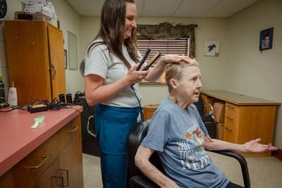 Staff member styling hair of a resident in a salon