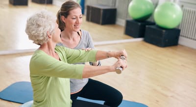 Resident exercising with a staff member in a bright activity room