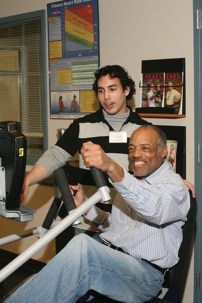 Resident exercising with staff assistance in a fitness area