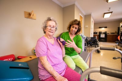 A caregiver assisting a senior resident with therapy exercises