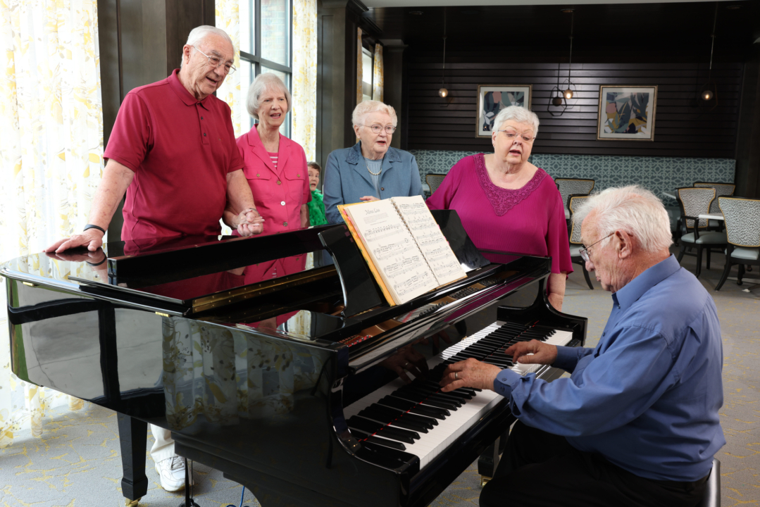 Residents singing around a grand piano in a common area