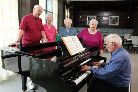 Seniors singing around a piano in a bright room
