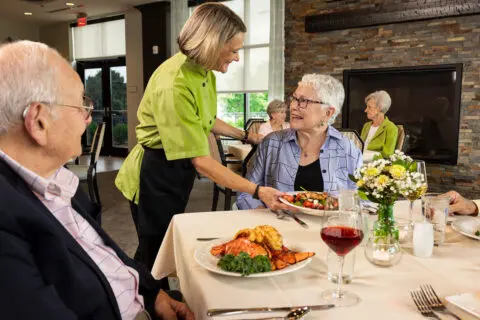 Residents enjoying a meal served by a staff member