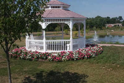 White gazebo surrounded by colorful flowers near a pond