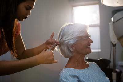 A stylist cutting a senior woman's hair in a salon