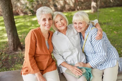 Three smiling senior women sitting together outdoors
