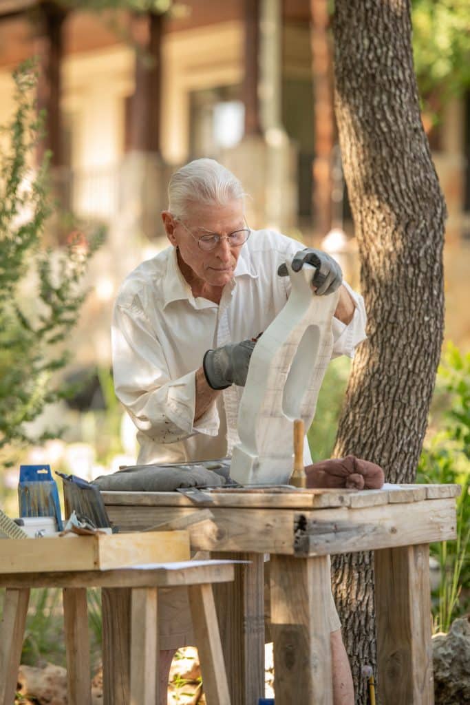 An elderly man sculpting outdoors in the garden
