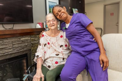 A caregiver and a senior resident smiling together in a cozy living area