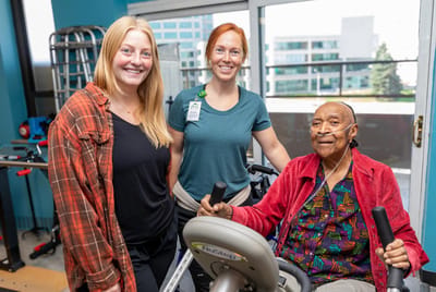 Three people in a therapy room during rehabilitation
