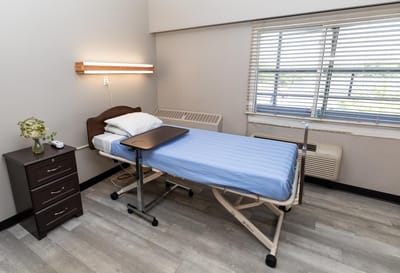 A private resident room with a bed and bedside table