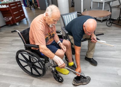 An elderly man in a wheelchair receiving assistance