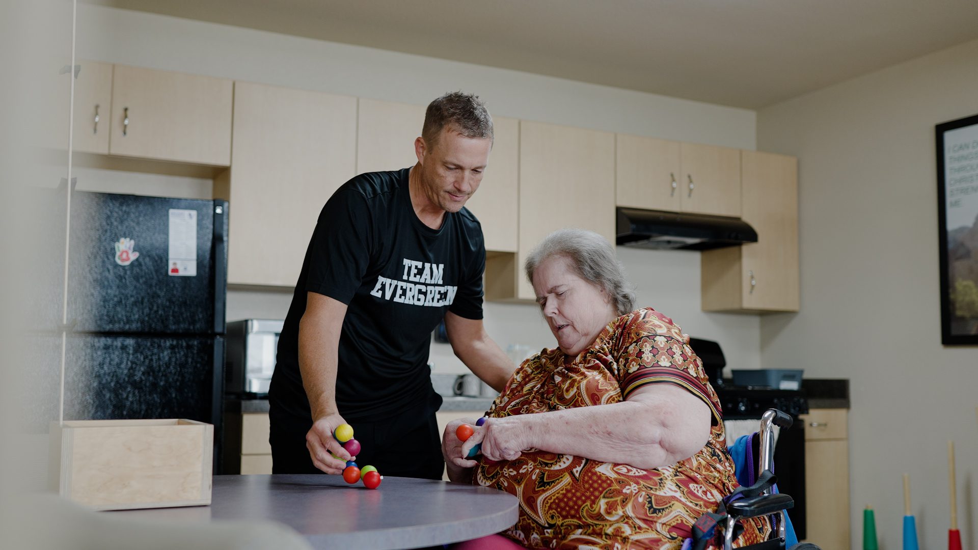 Staff assisting a resident with a colorful activity in a common area