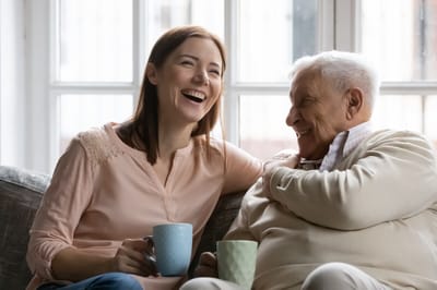 A caregiver and an elderly man sharing a laugh indoors