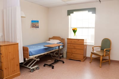 A private resident room with a bed, dresser, and flower vase