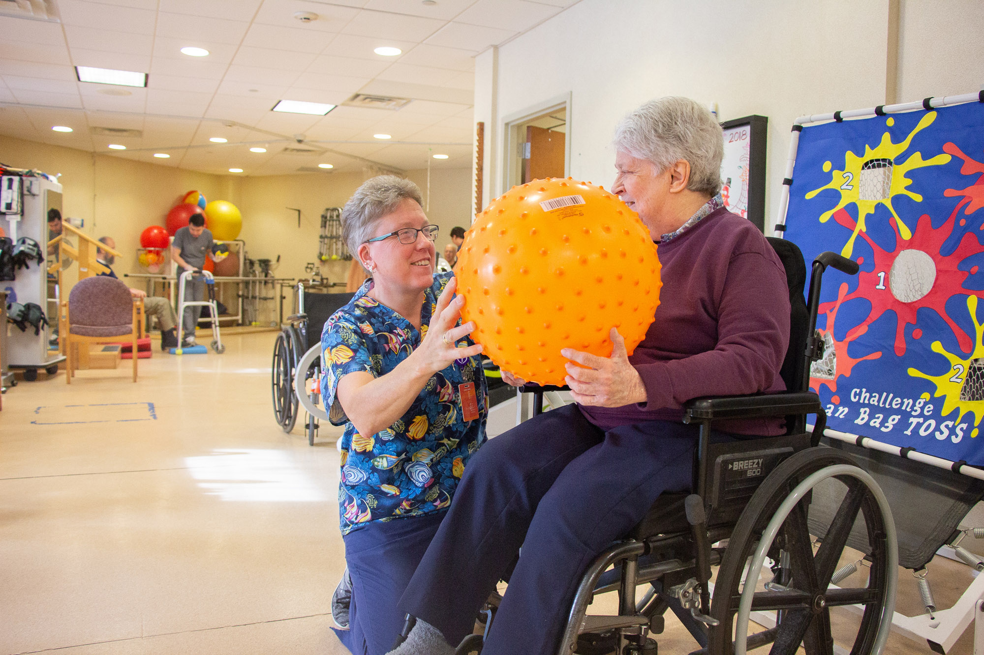 Therapist assisting a resident with a therapy ball in an activity room