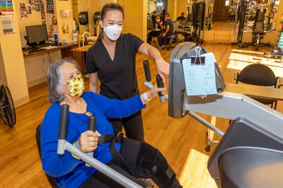 Staff assisting resident with exercise equipment in an activity room