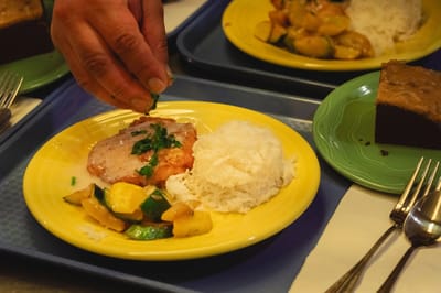 A hand garnishing a dinner plate in a dining room