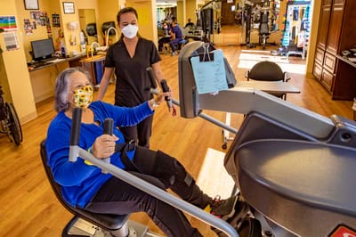 Resident exercising with staff assistance in an activity room