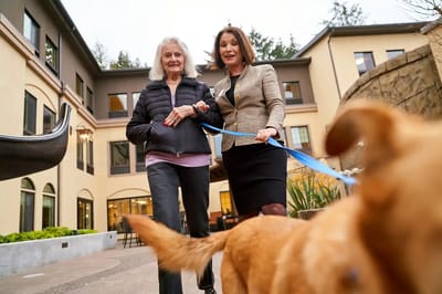Resident and staff member walking a dog in outdoor space