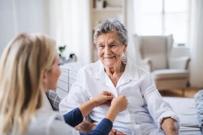 Caregiver assisting a smiling senior woman indoors