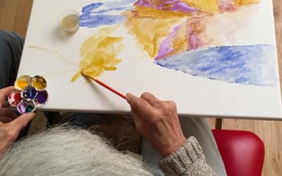 A senior resident painting at a table with watercolors