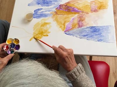 An elderly person painting on a canvas