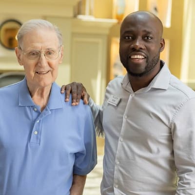 An elderly resident poses with a staff member in the lobby