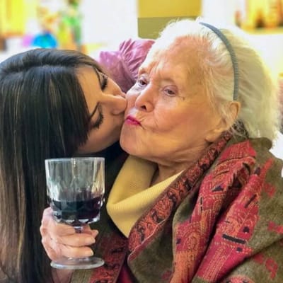 An older woman enjoys a kiss from a younger woman, both smiling.