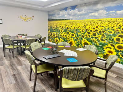 Bright activity room with sunflower mural and tables