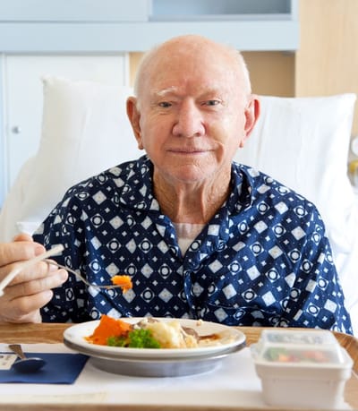 Resident enjoying a meal in a hospital bed