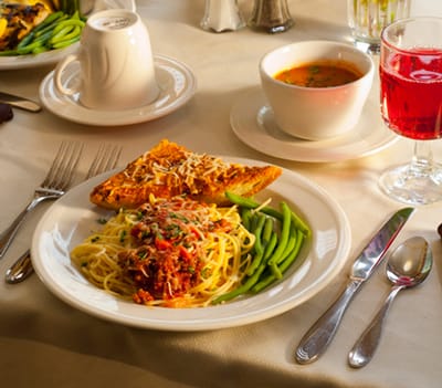 Plated meal with pasta, greens, and soup on a dining table