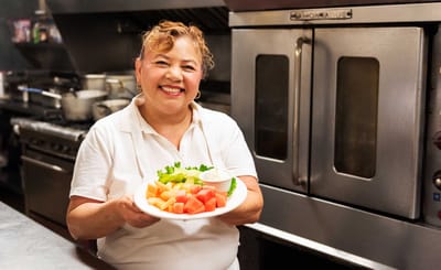 Staff member smiling while holding a plate of colorful fruit