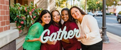 Four staff members holding a 'Gather' sign outdoors