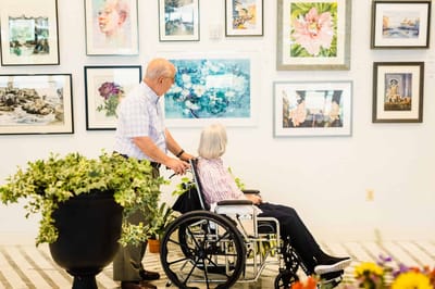 A resident in a wheelchair admiring artwork with a staff member.