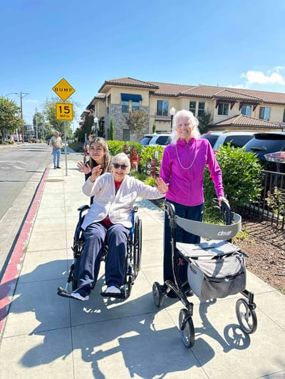 Residents enjoying a walk outside with staff assistance