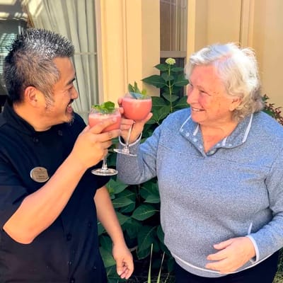 A resident and staff member toasting with drinks outdoors