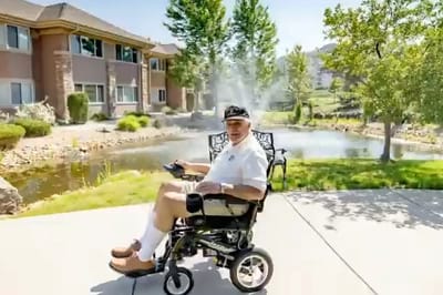Resident in a wheelchair by a pond outside the facility