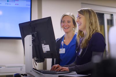 Two healthcare staff smiling at a computer in a facility
