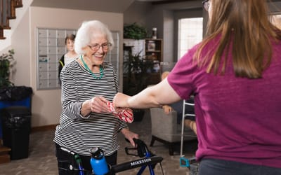 An elderly resident receiving a gift from staff in a common area