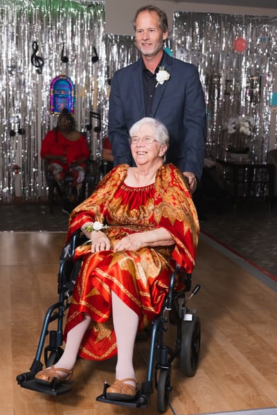 A resident in a colorful outfit being assisted at an event