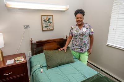 A caregiver in a resident room with a neatly made bed
