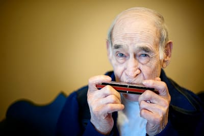 An elderly man playing a harmonica indoors