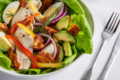 A colorful salad with chicken, avocado, and bacon