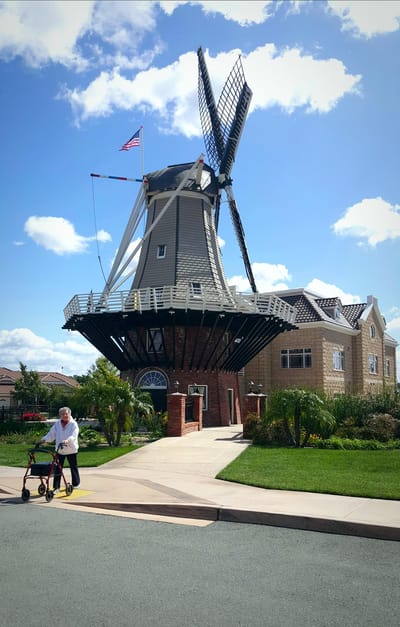 A senior man walking past a unique building with a windmill.